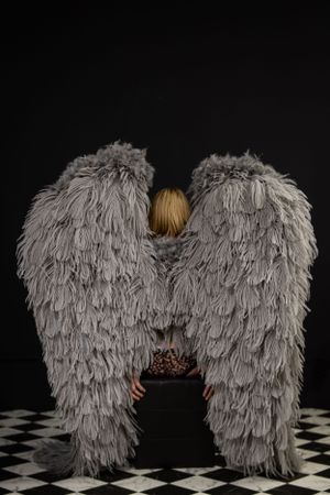 Large gray feathered angel wings photographed against black background on checkered floor.