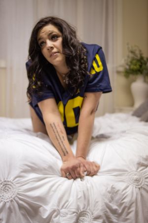 Person in blue sports jersey poses on white bedding.