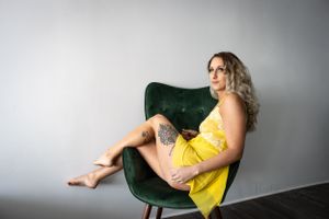 Woman in yellow dress poses confidently on green velvet chair.