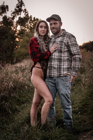 Couple in plaid shirts pose together in a rustic outdoor setting at sunset.
