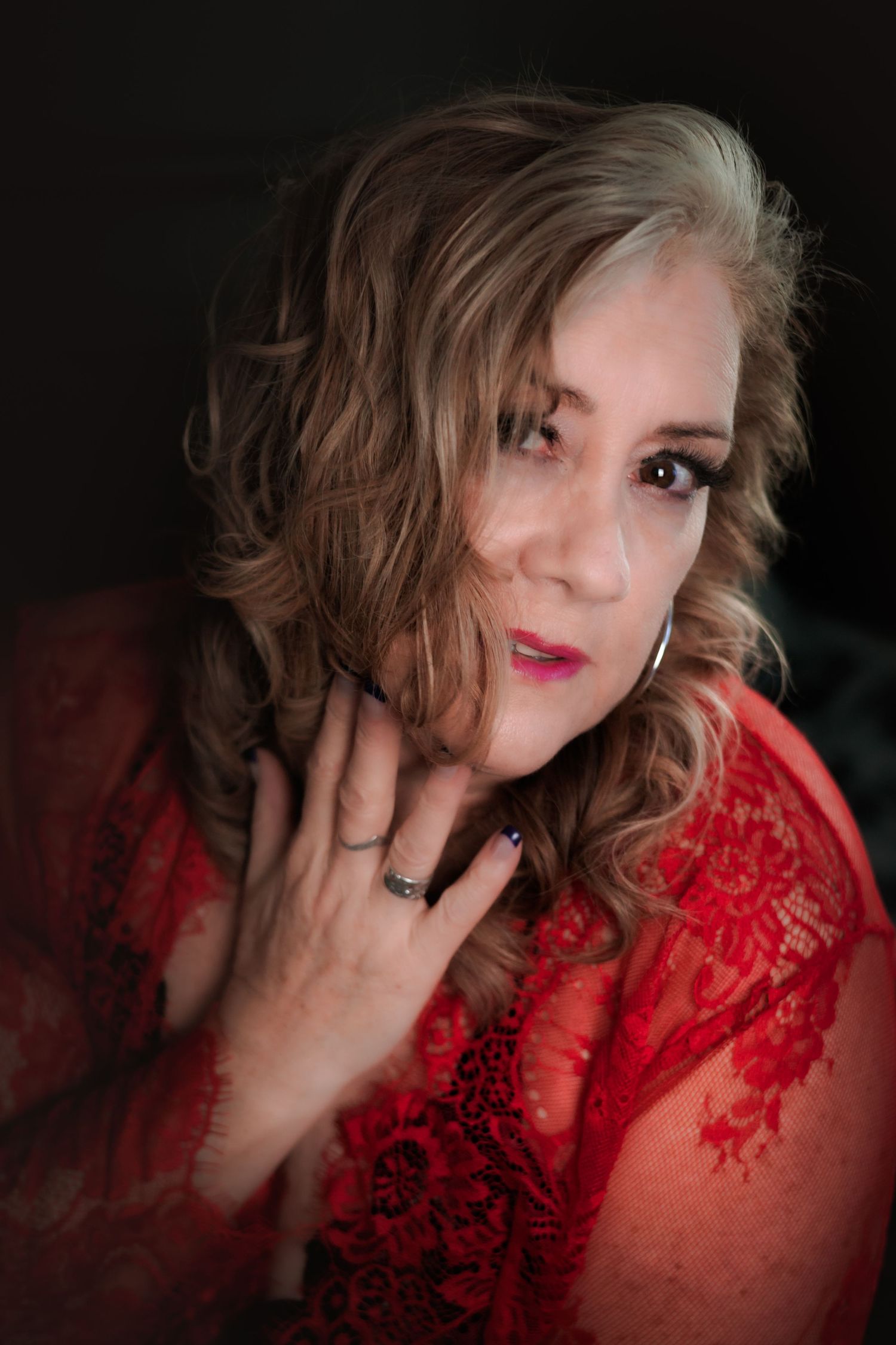 Close-up portrait of woman in red lace top with styled hair.