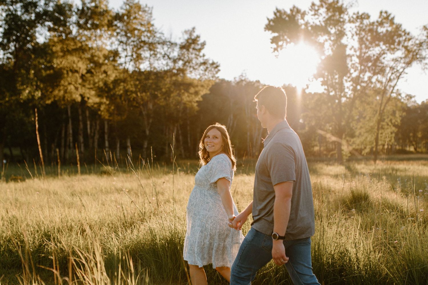 A couple shares an intimate moment in a sunlit meadow at golden hour.