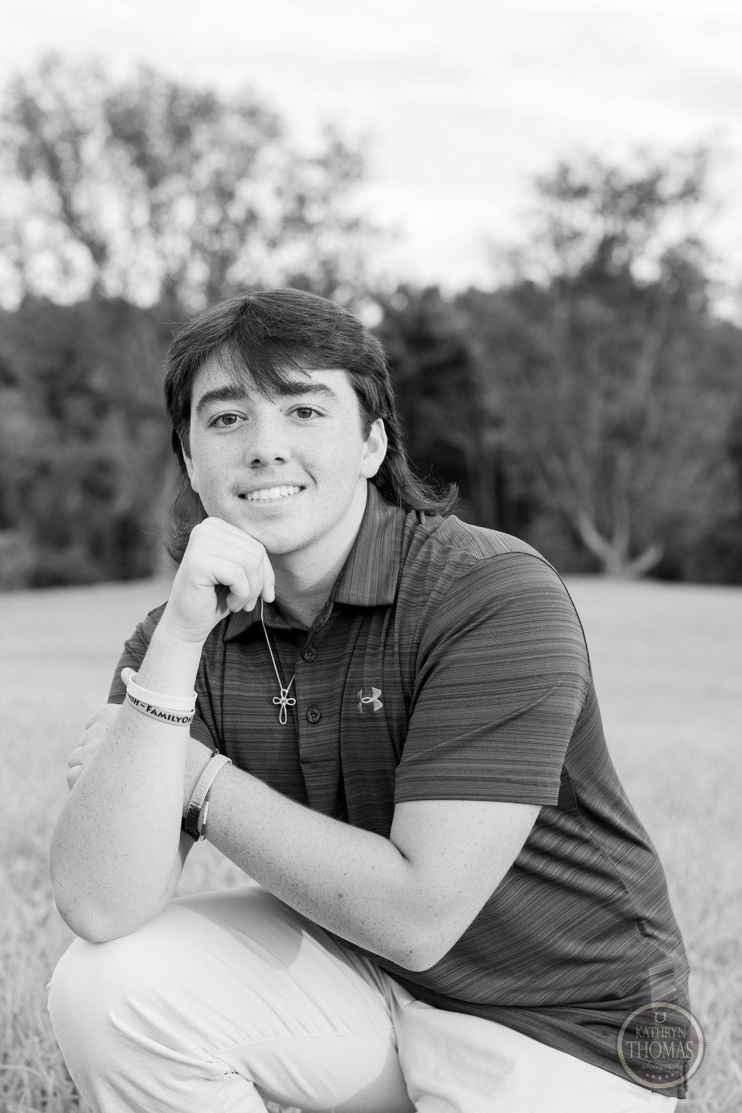A black and white portrait of someone in a polo shirt posing thoughtfully outdoors.