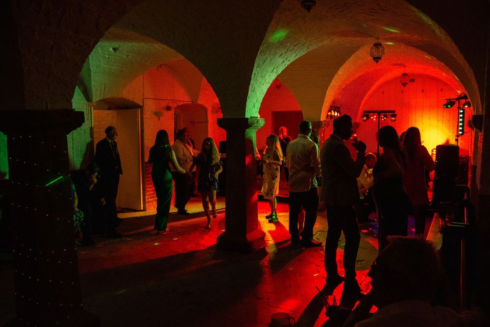 Silhouettes of party guests dancing under dramatic red and green lighting in an arched venue.