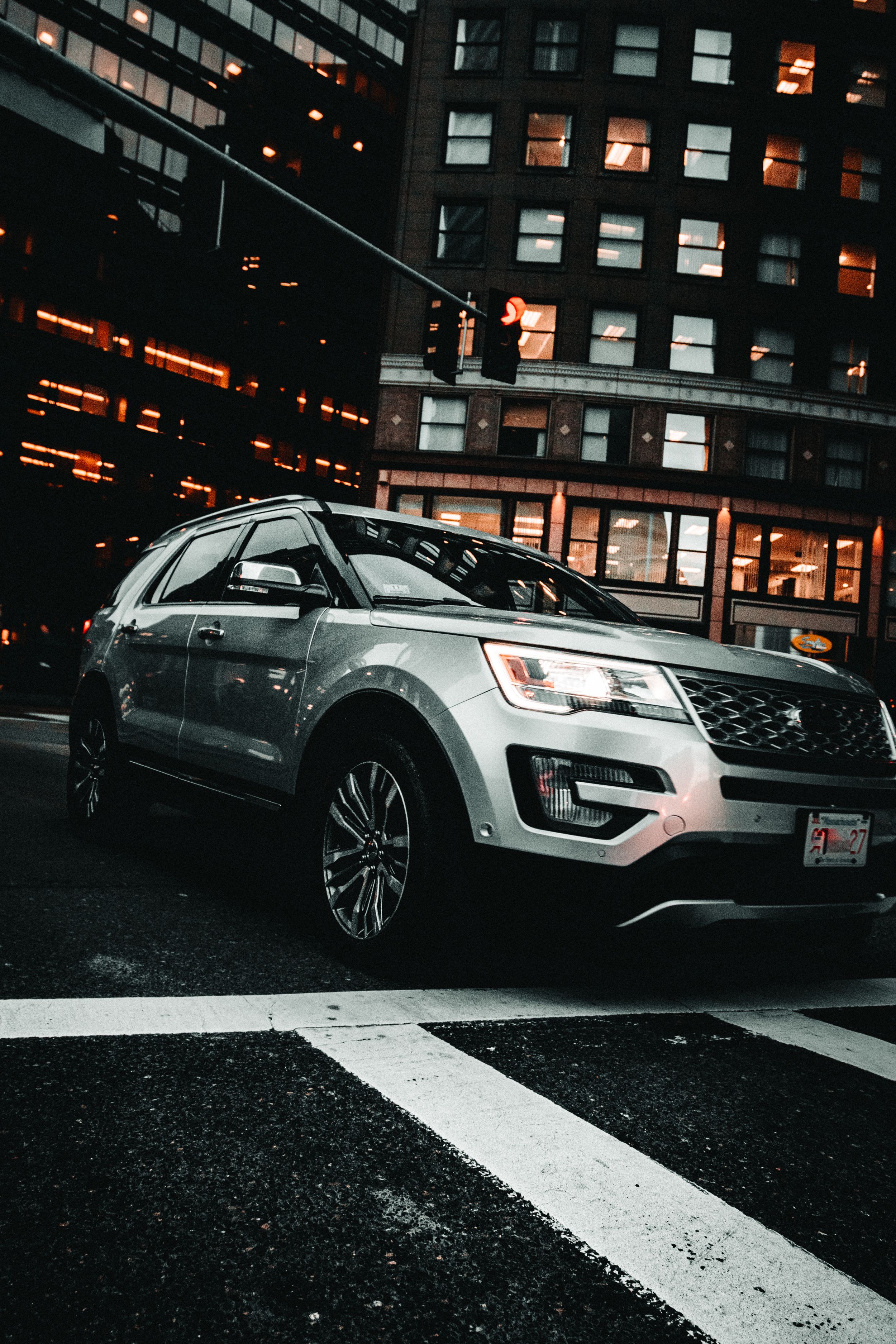 Silver Ford Explorer SUV parked on a city street at night with illuminated buildings in the background.