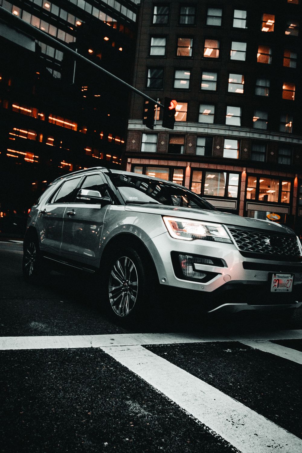 Silver Ford Explorer SUV parked on a city street at night with illuminated buildings in the background.