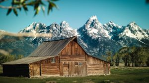 Historic wooden barn with snow-capped Grand Teton mountains in background.