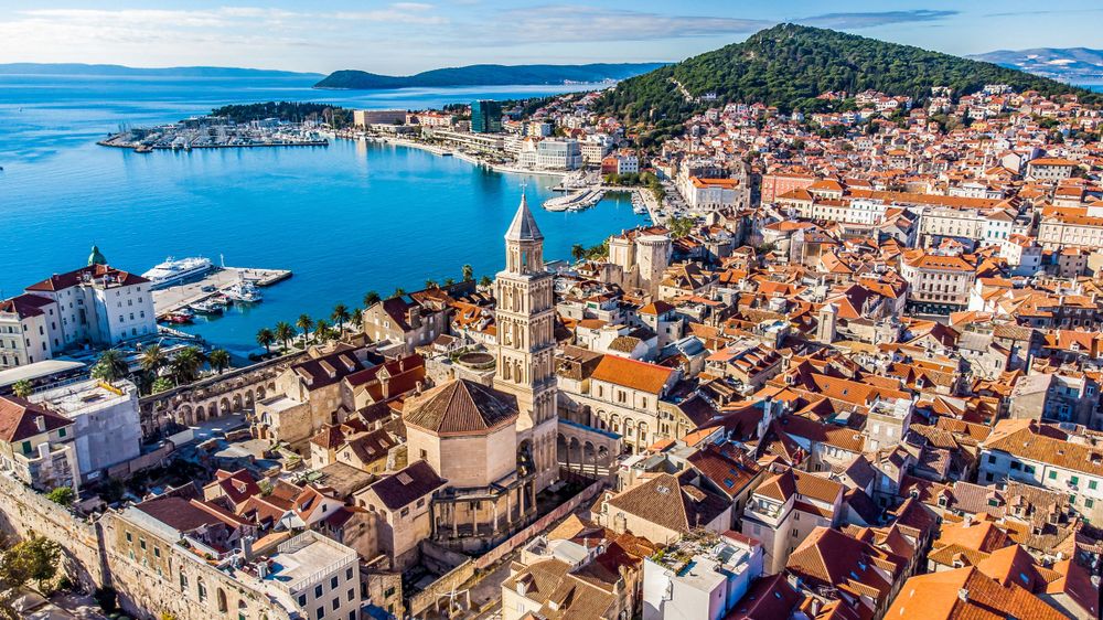 Aerial view of Split's historic old town showcasing terracotta roofs and the iconic cathedral bell tower by the harbor.
