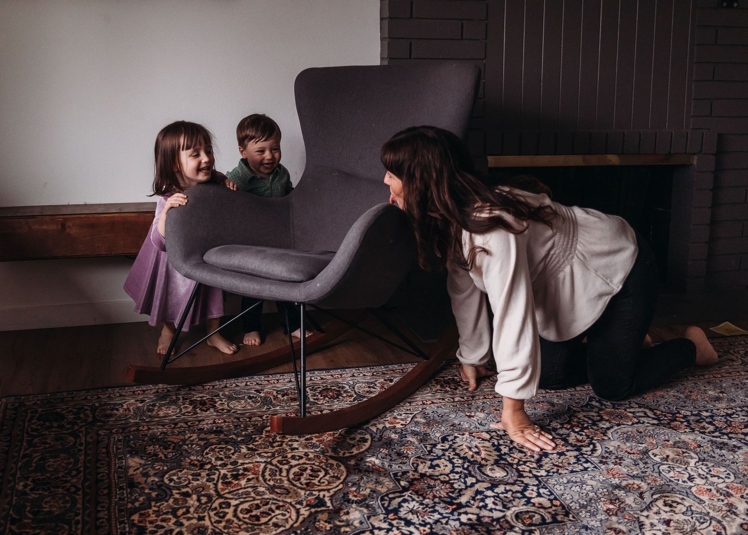 Playful moment around grey chair on patterned rug in home interior.