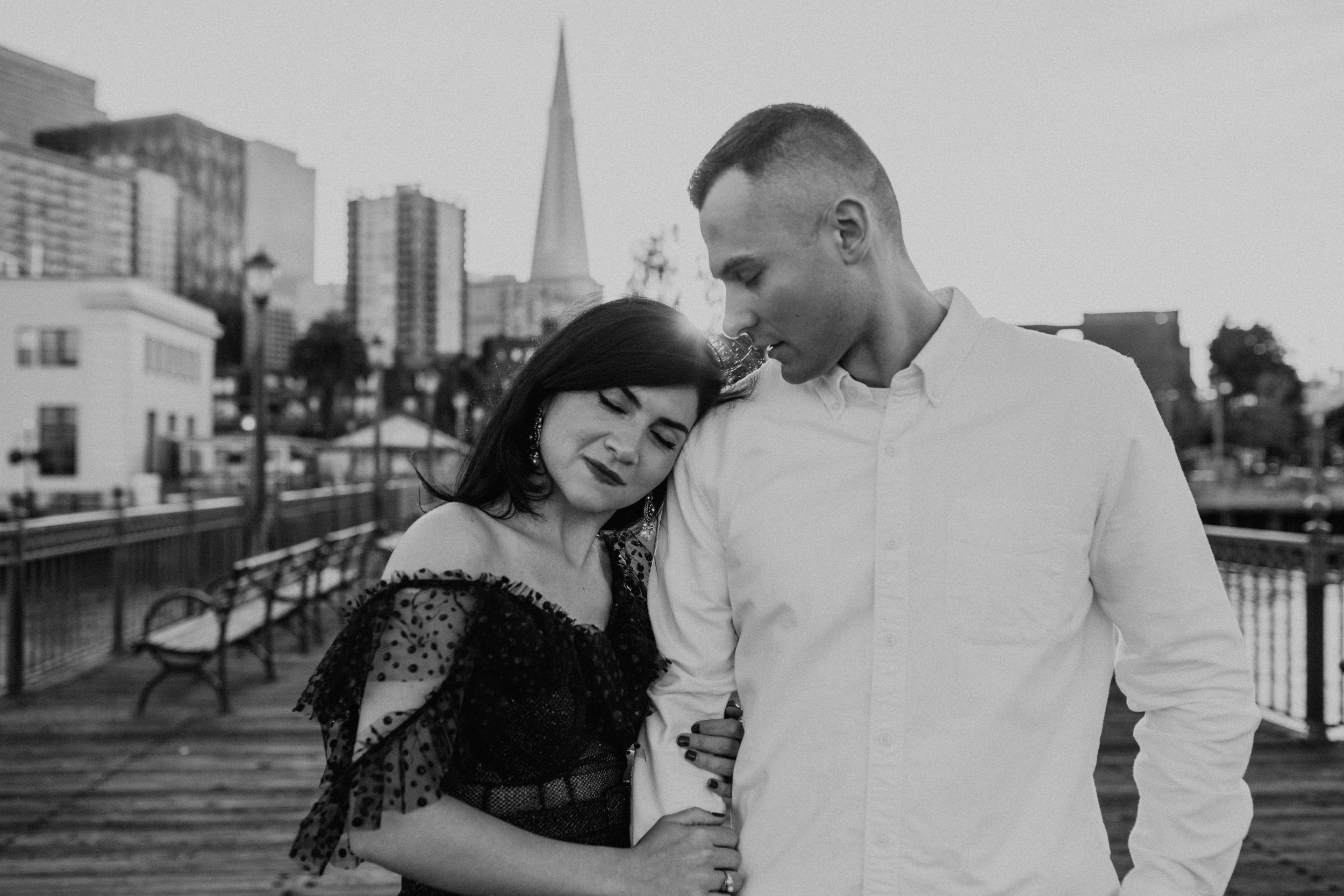 A romantic black and white portrait of a couple embracing on a waterfront pier.