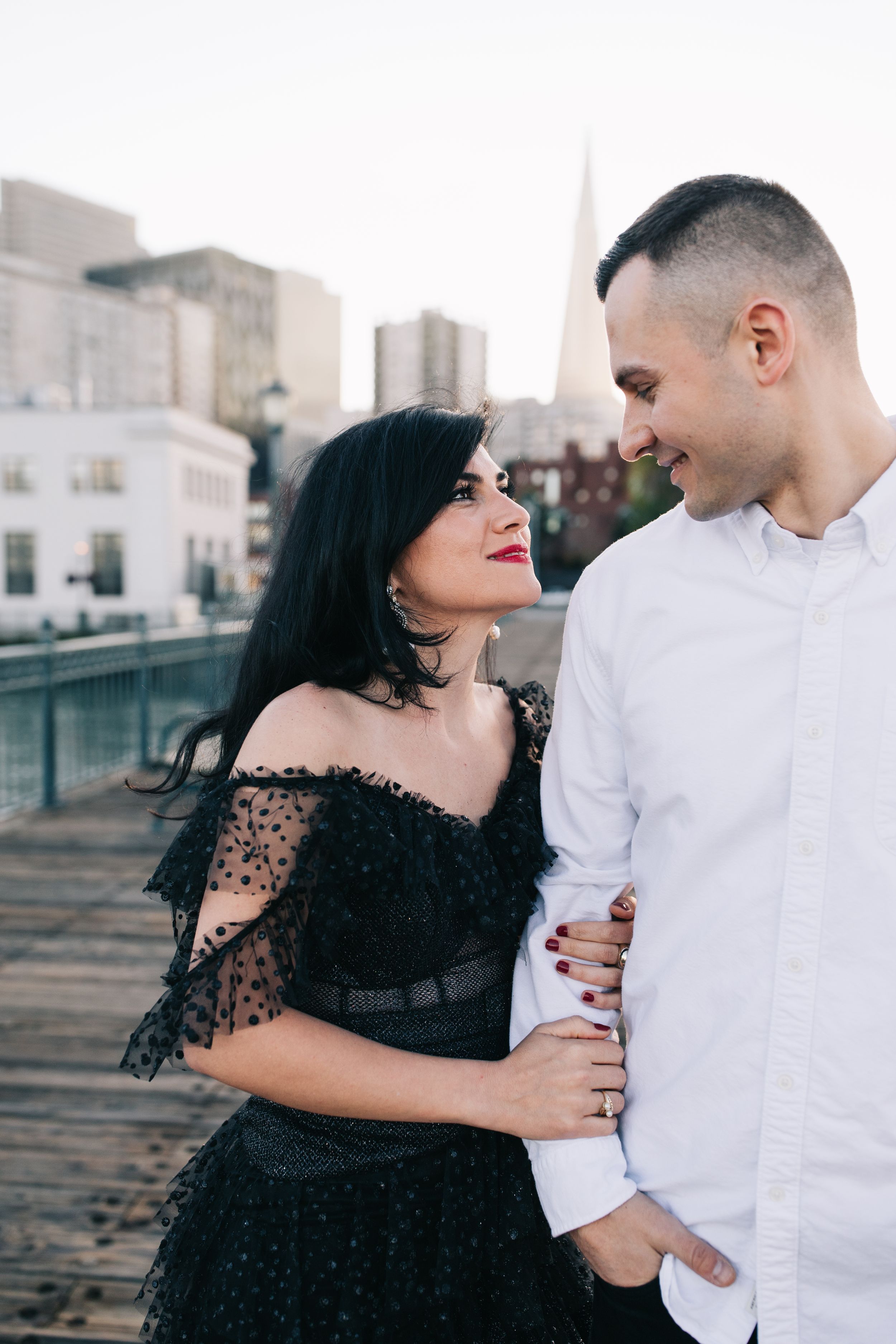 A couple shares an intimate moment on a pier with the San Francisco skyline in the background.