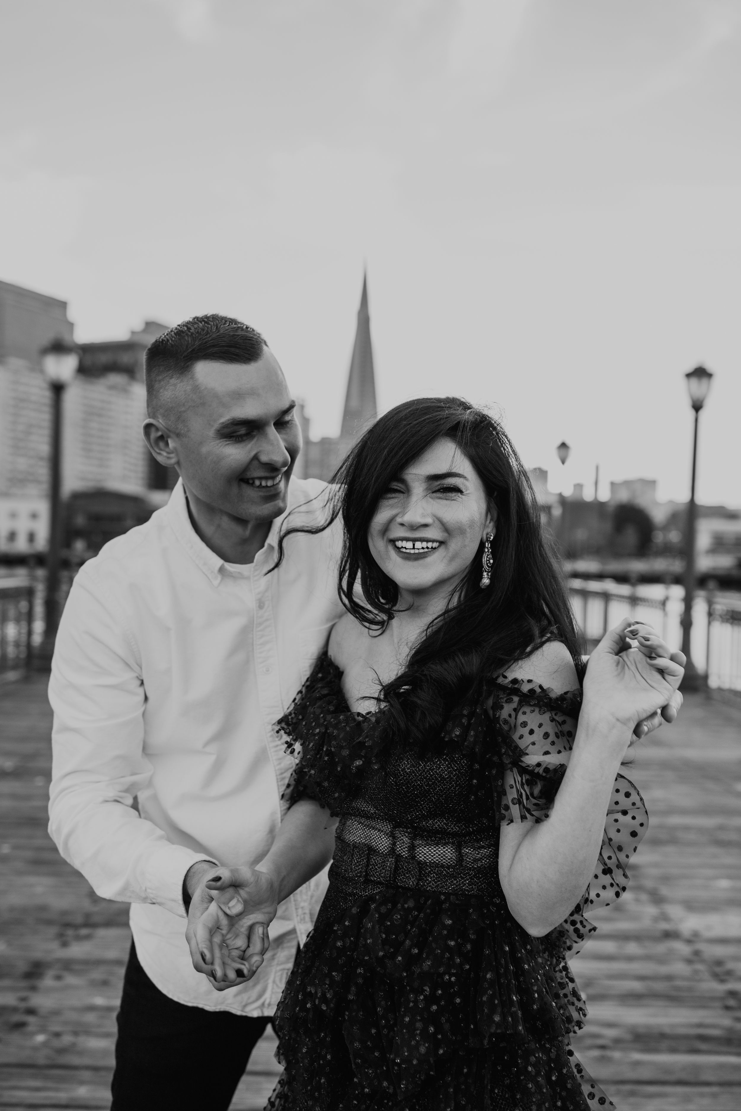 A joyful black and white portrait of a couple laughing together on a pier.
