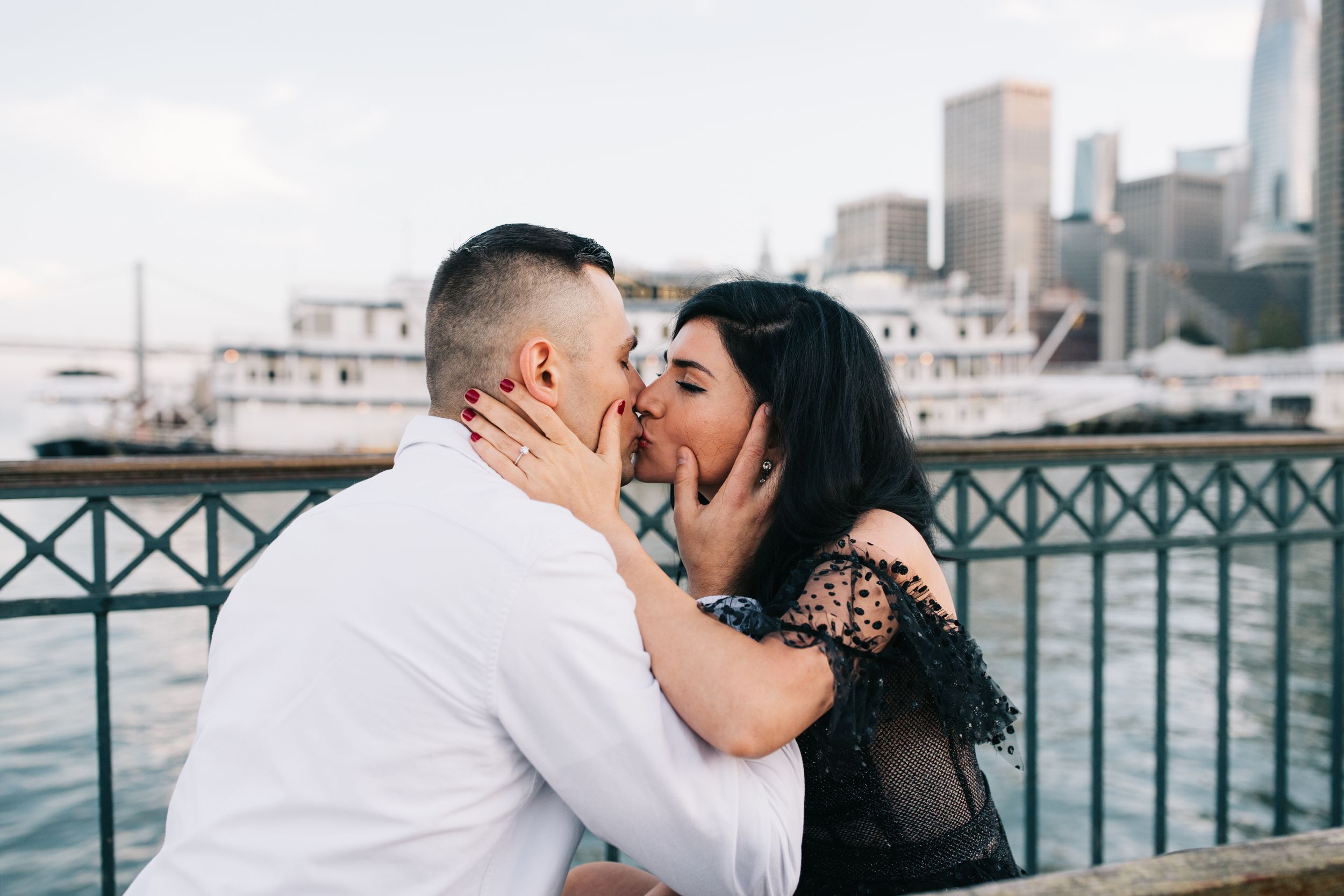 A romantic moment captured on a pier with the San Francisco Bay and boats in the background.