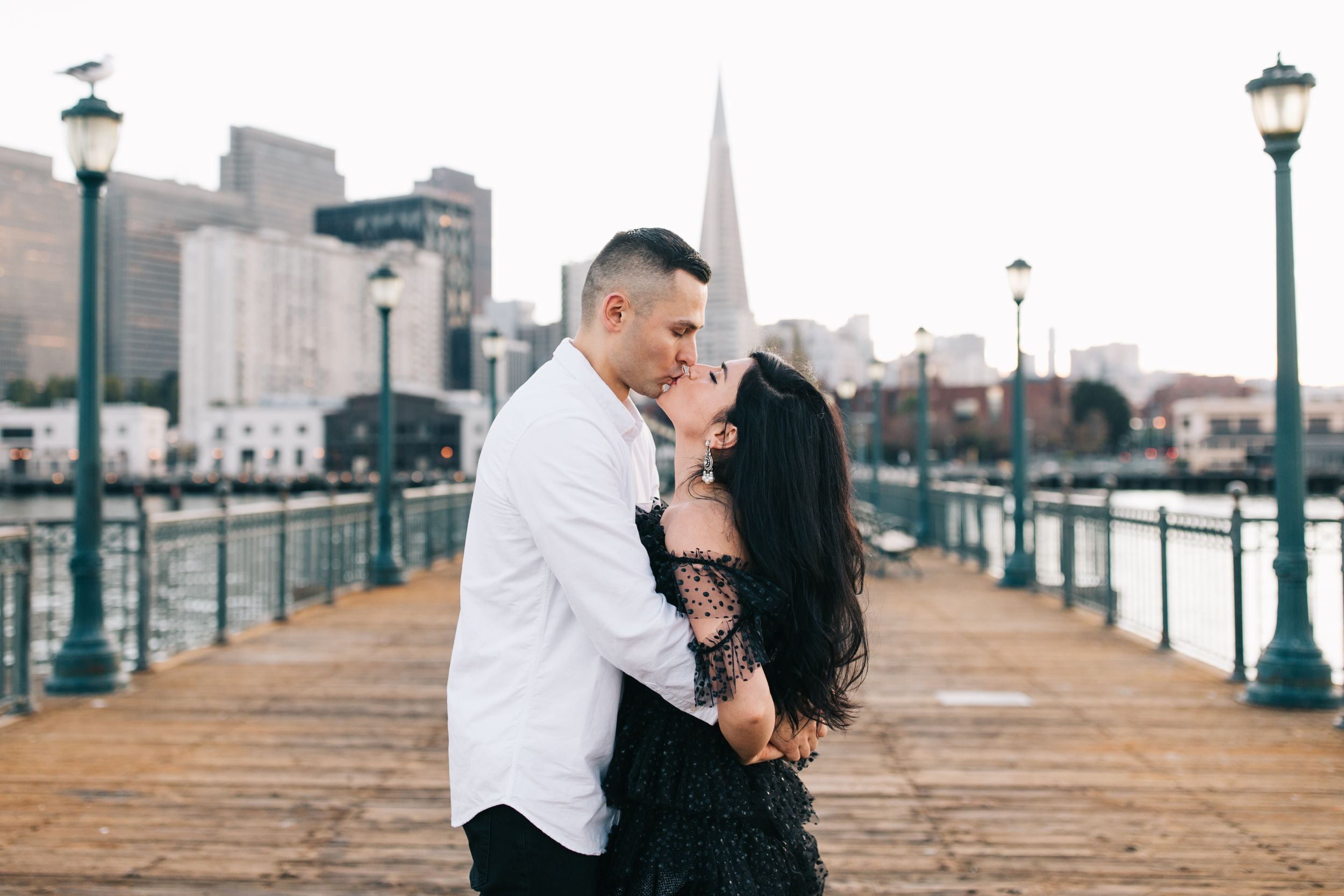 A romantic moment shared on a wooden pier with the San Francisco skyline and Transamerica Pyramid in the background.