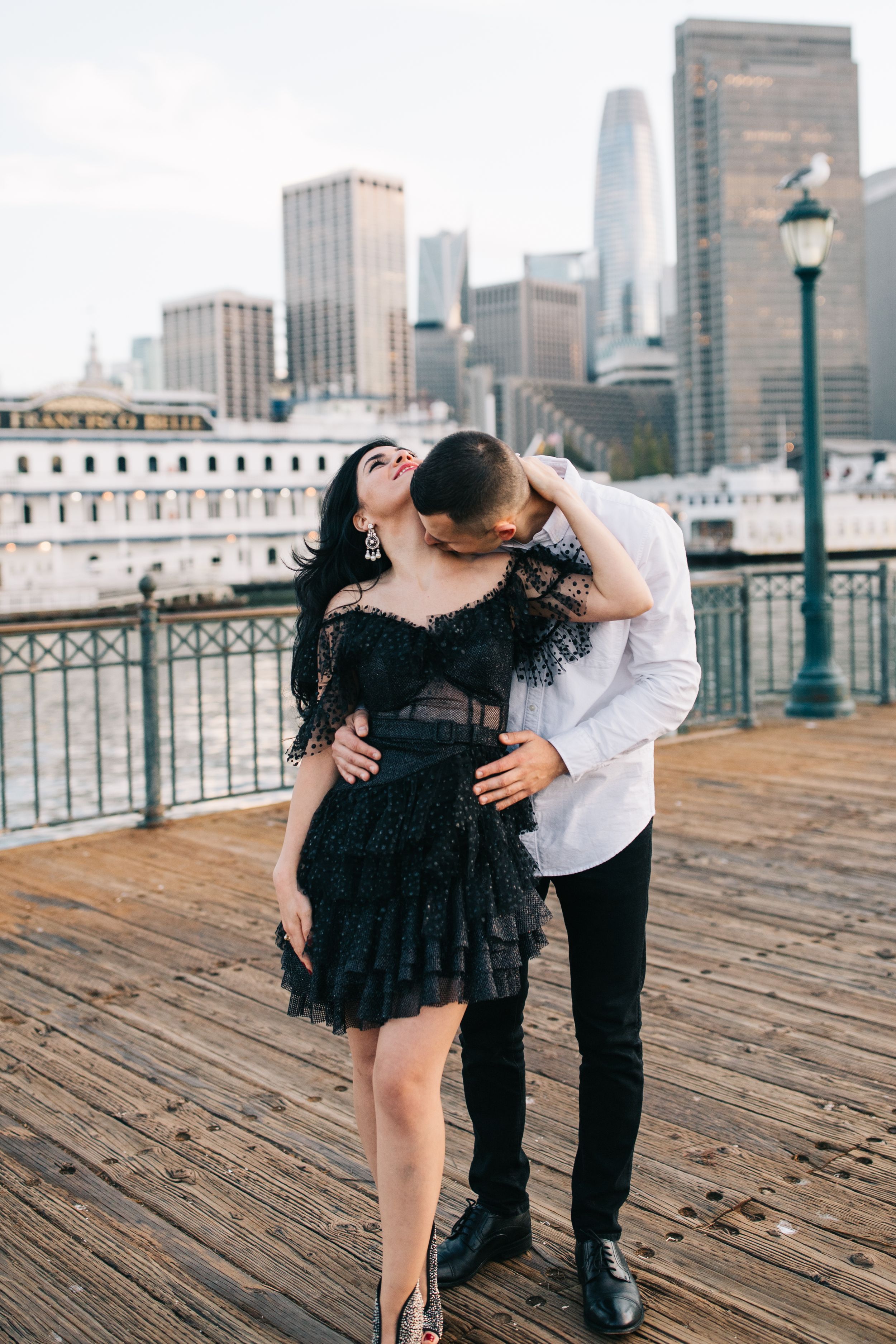 An intimate moment shared on a San Francisco pier with the Financial District towers in the background.