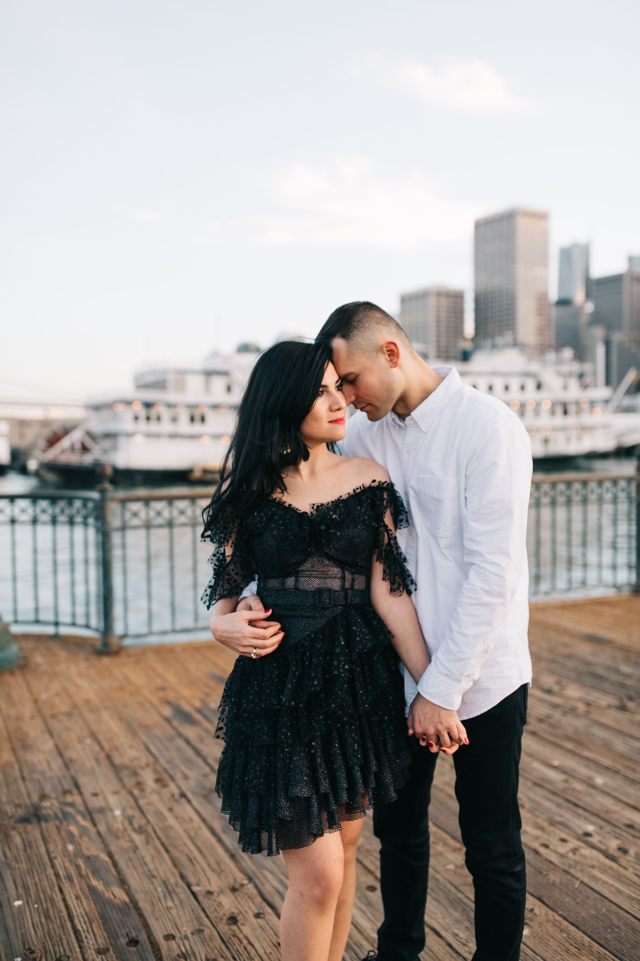 A tender moment between a couple in contrasting black and white outfits on a waterfront pier.