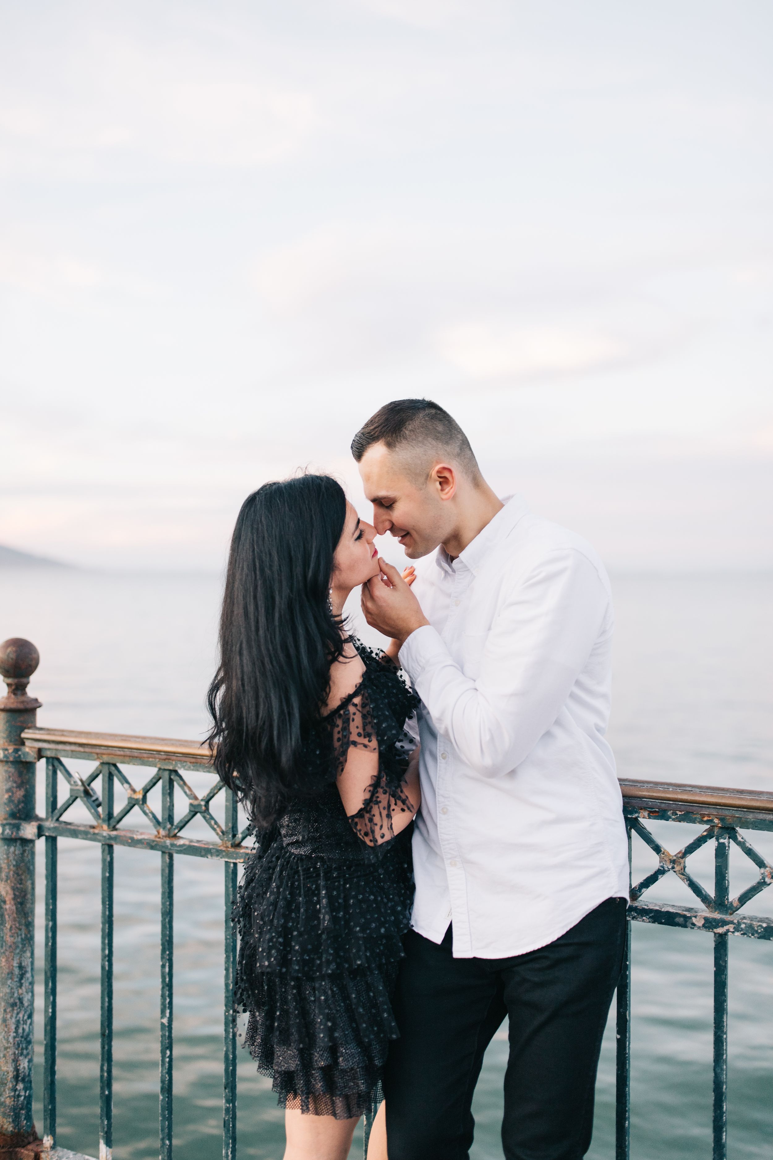 Romantic couple sharing an intimate moment on a pier overlooking the bay at sunset.