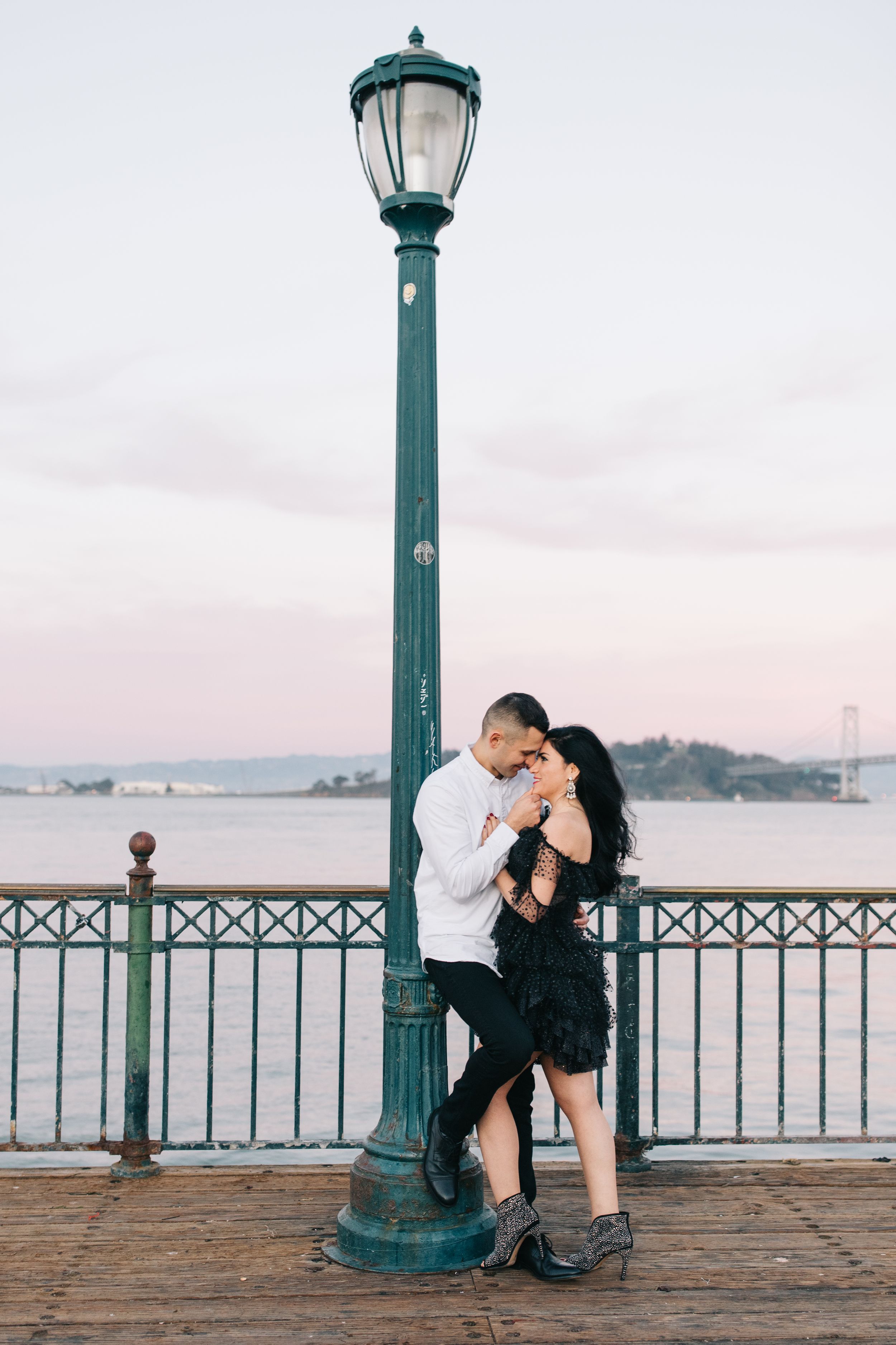 Intimate moment between couple at vintage waterfront lamp post during sunset.