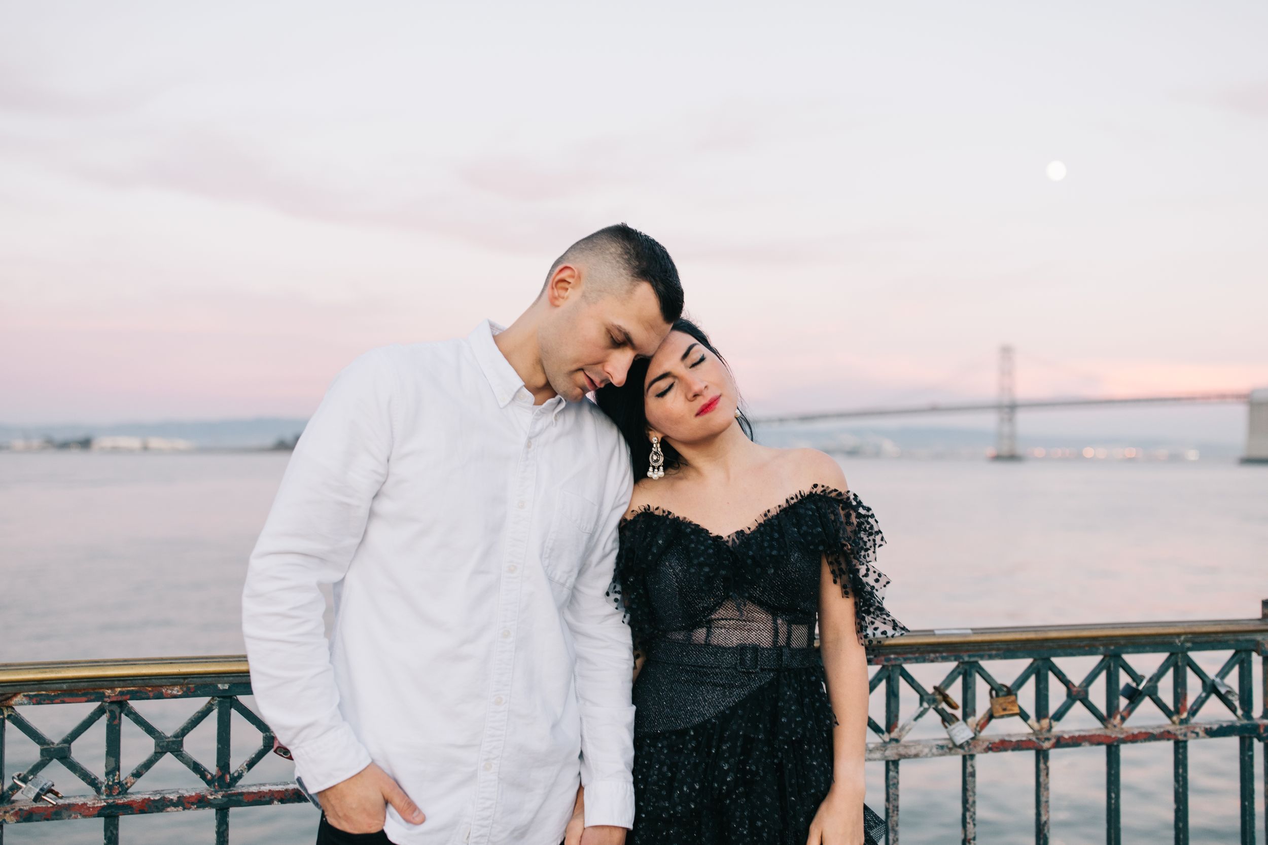 Couple in contrasting black and white outfits share tender moment on waterfront pier.