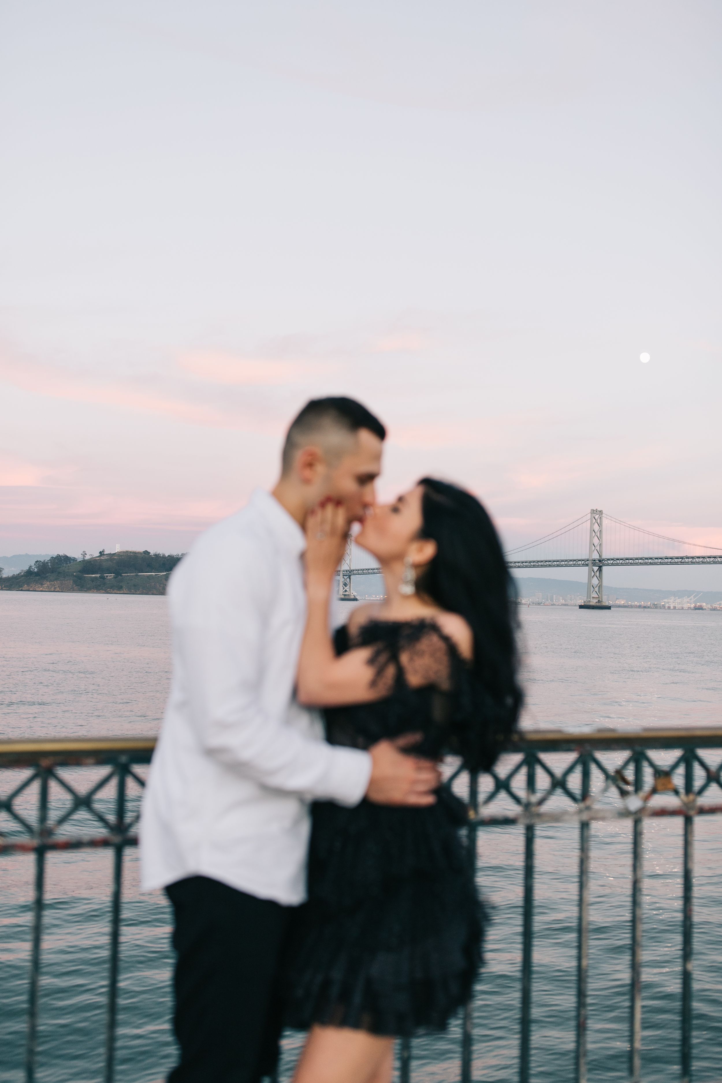 Intimate embrace between couple on pier during sunset with bay views.