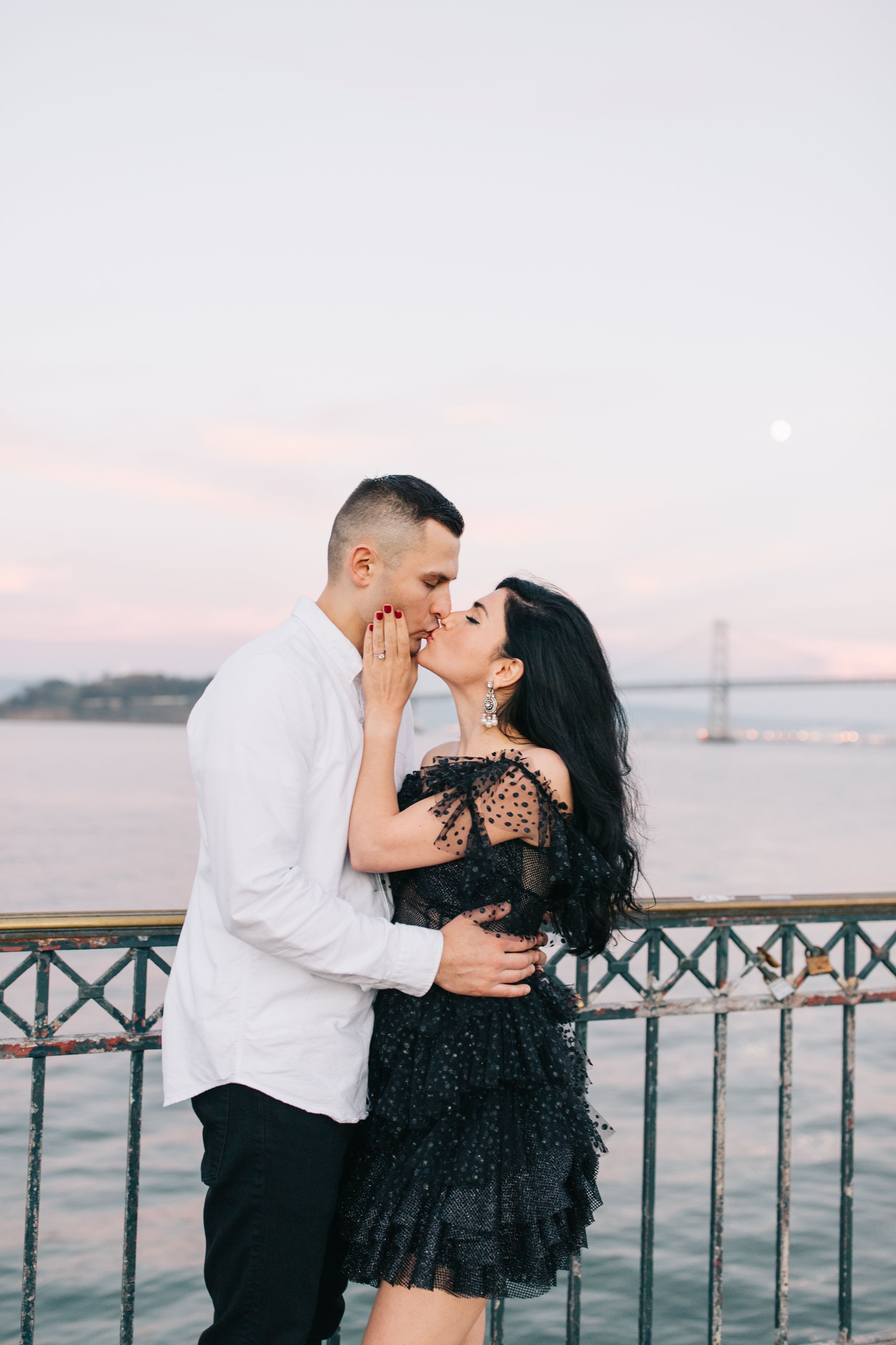 Romantic couple sharing an intimate moment at sunset with the Bay Bridge visible in the background.
