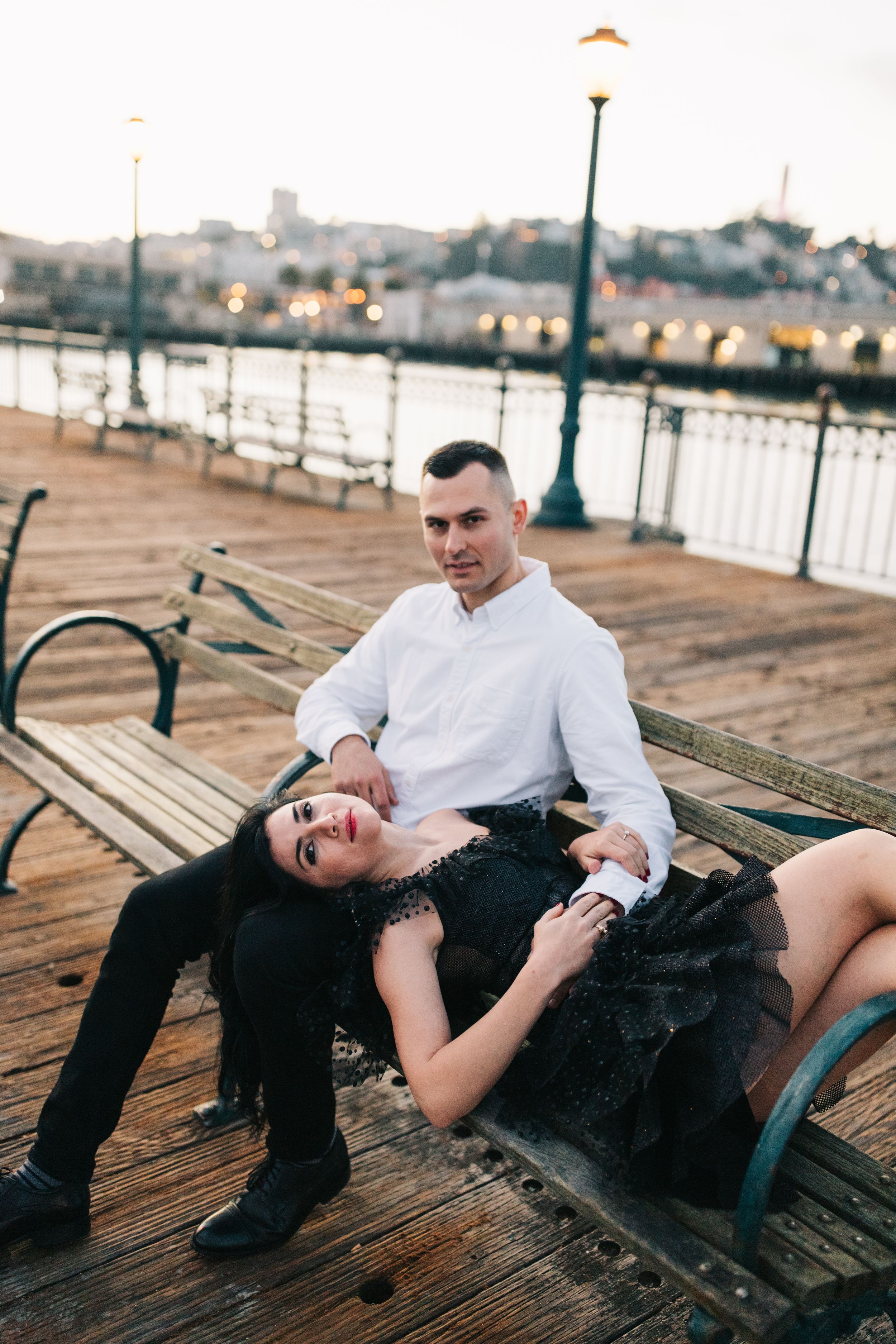Couple relaxing on wooden bench along scenic waterfront pier at dusk.