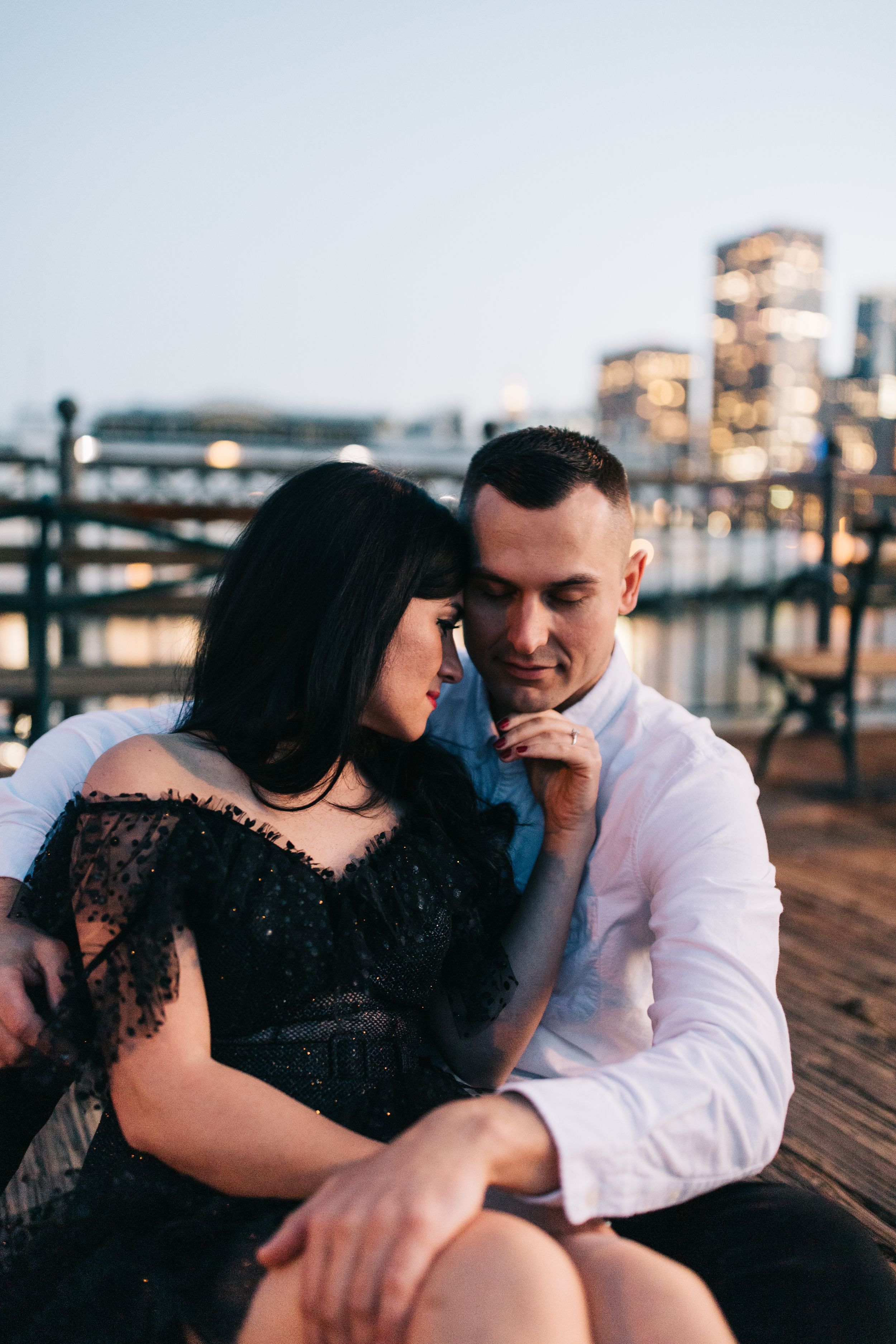 Intimate portrait on waterfront pier with glowing city lights and romantic evening atmosphere.