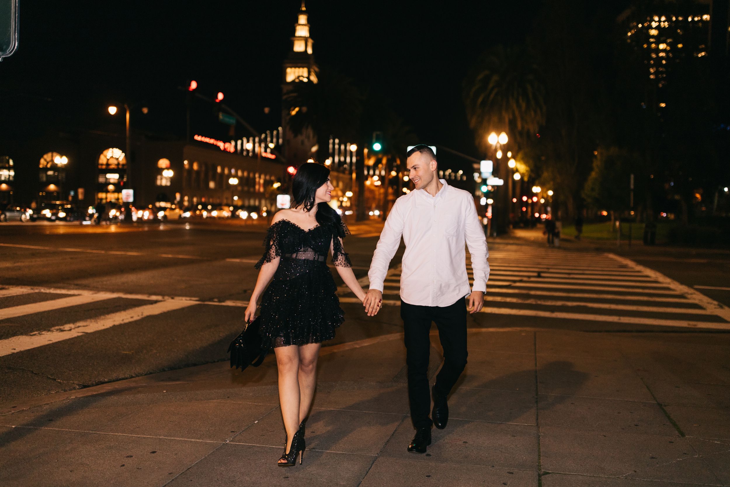 Stylish couple walking hand in hand through city streets at night with historic architecture.