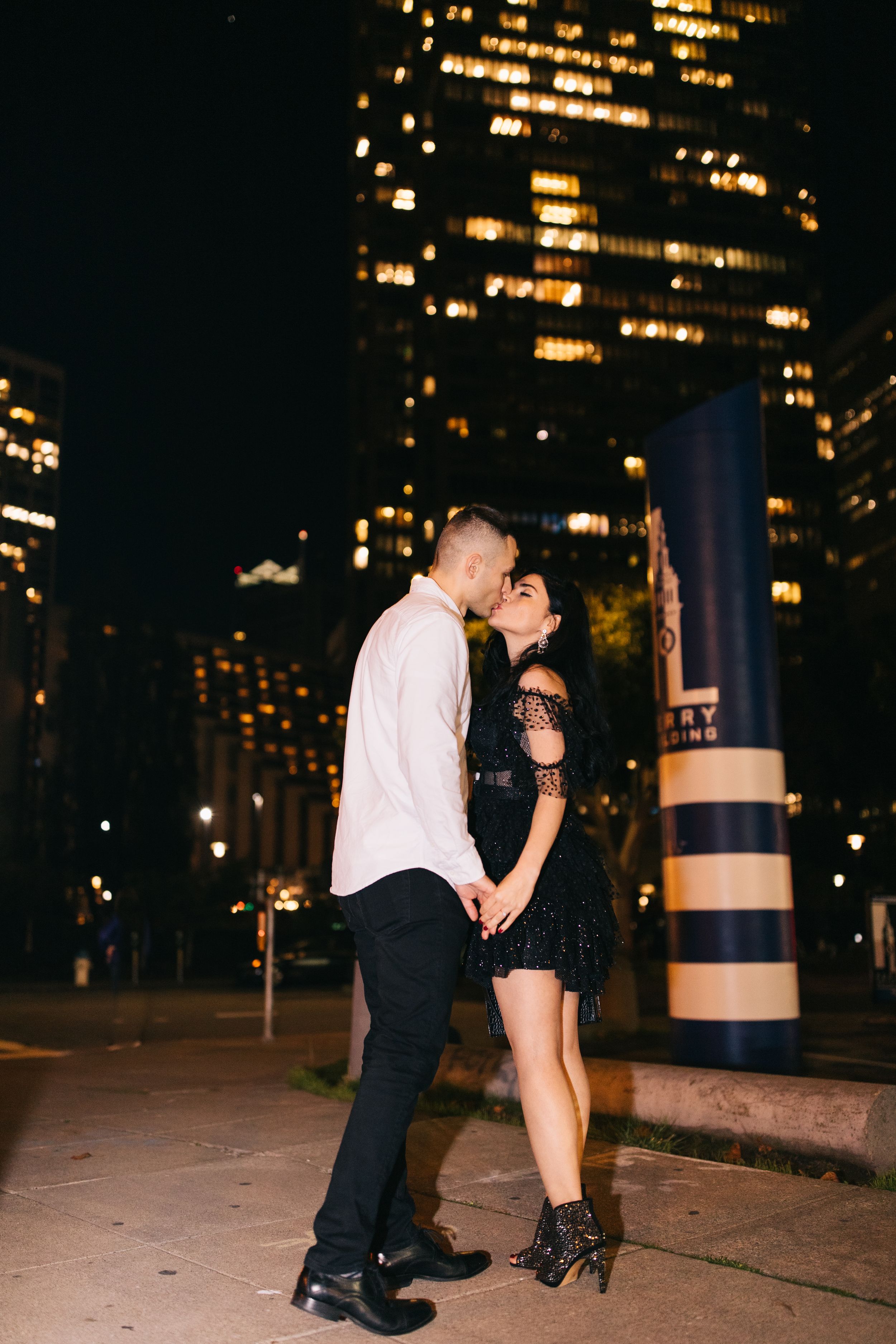 Intimate nighttime moment against backdrop of illuminated skyscrapers and city lights.