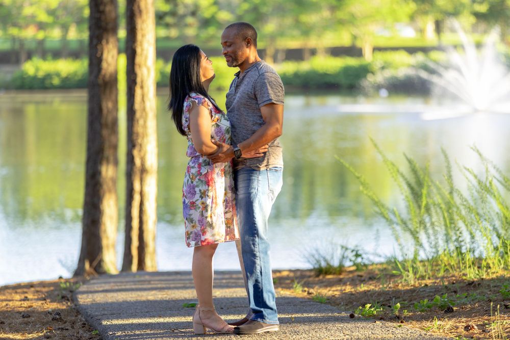 Romantic engagement photoshoot along a serene lake with lush greenery and natural sunlight.