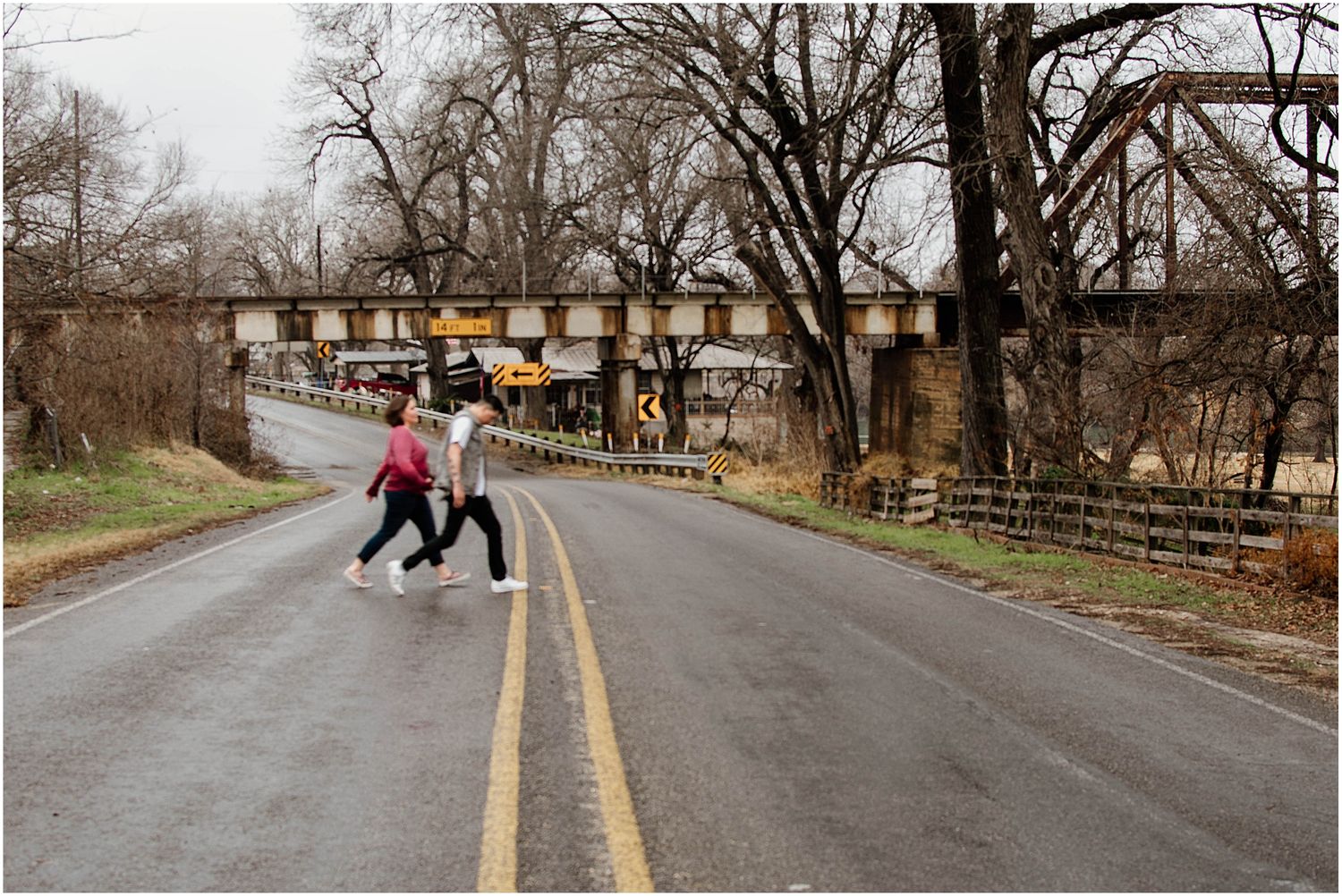 Two people walking together on curved road under rustic bridge during winter.