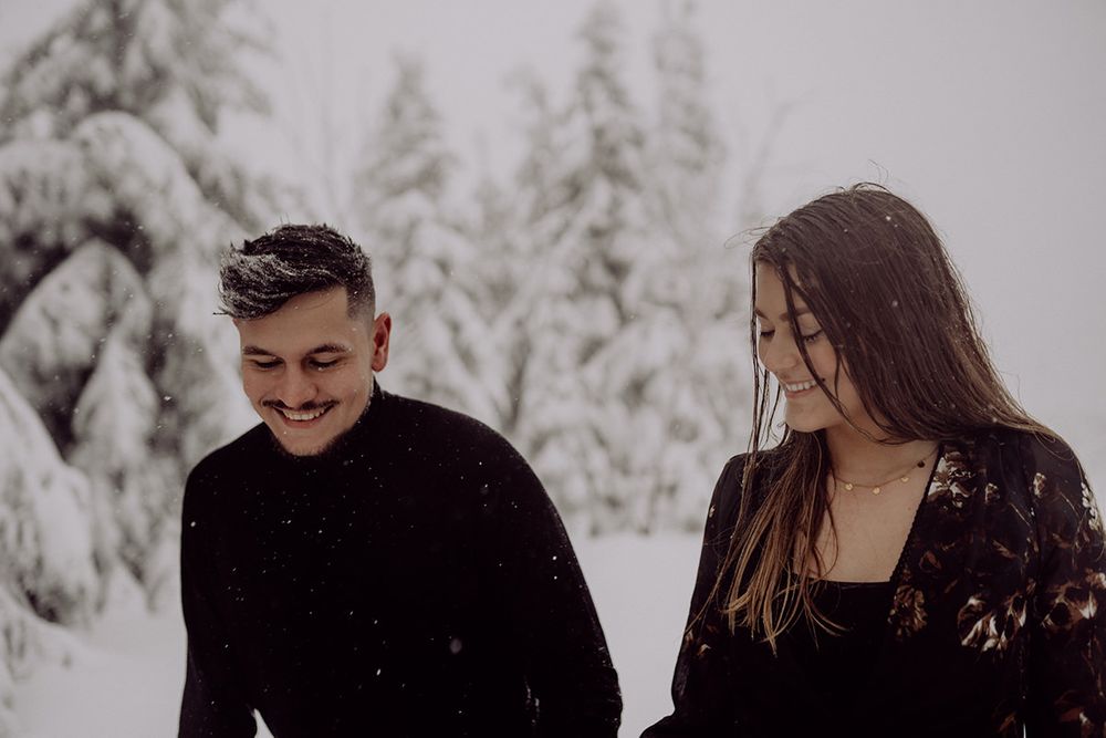 A couple shares joyful laughter while walking in a snow-covered winter forest.