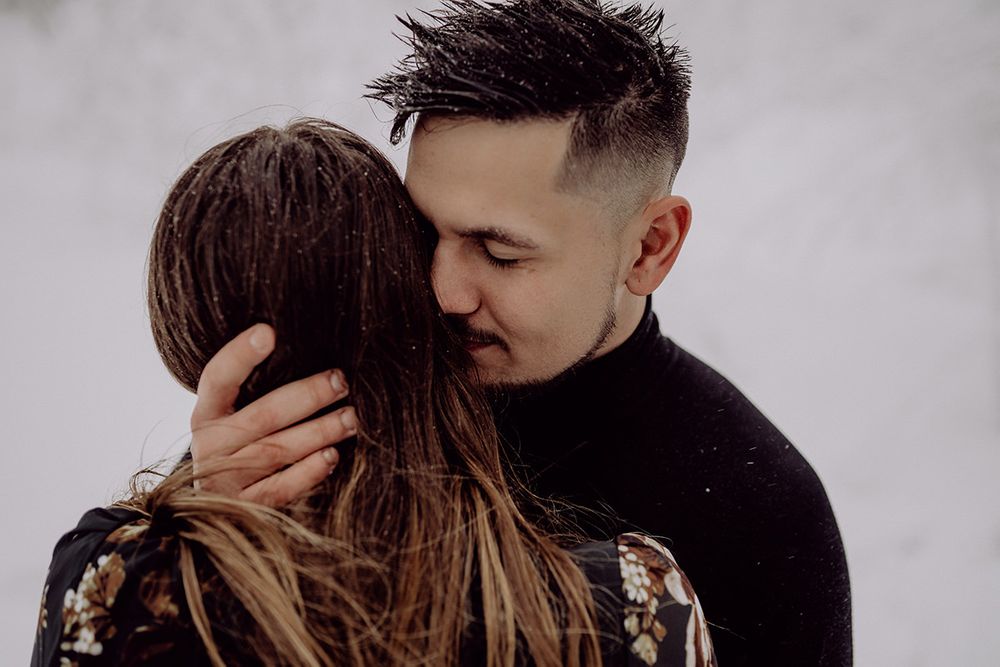 A tender moment between a couple in winter clothes with snowflakes falling around them.
