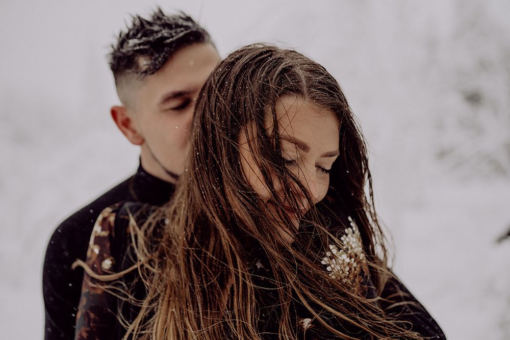 A couple shares an intimate winter moment with snow falling in their hair.