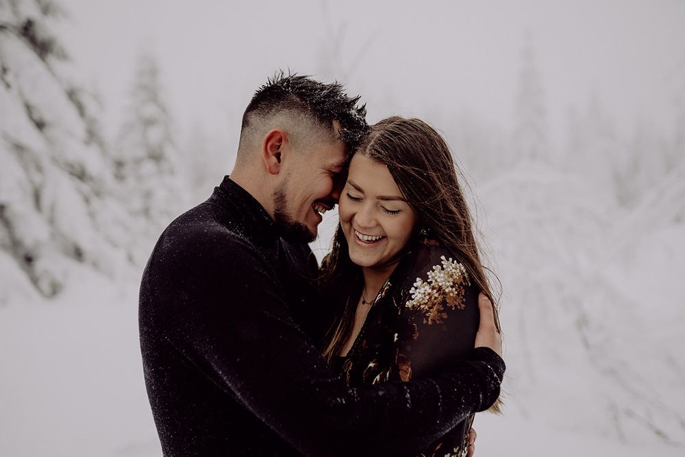 A tender moment between a couple sharing an intimate embrace in a snowy forest landscape.