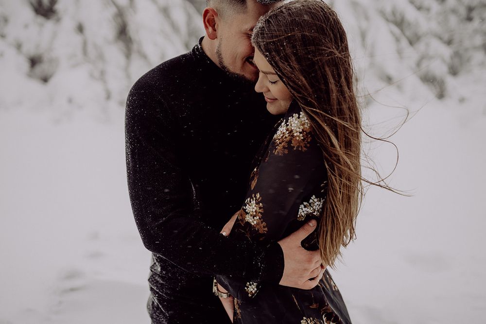 A loving couple shares an intimate moment in the snow while wearing winter attire.