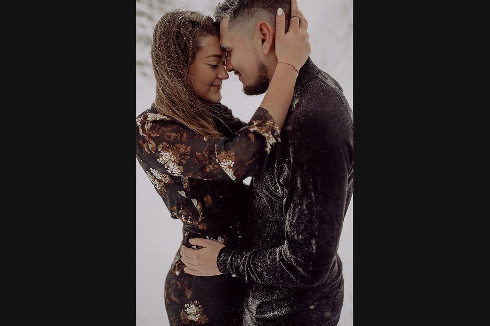 A couple embraces closely while wearing winter attire against a snowy background.