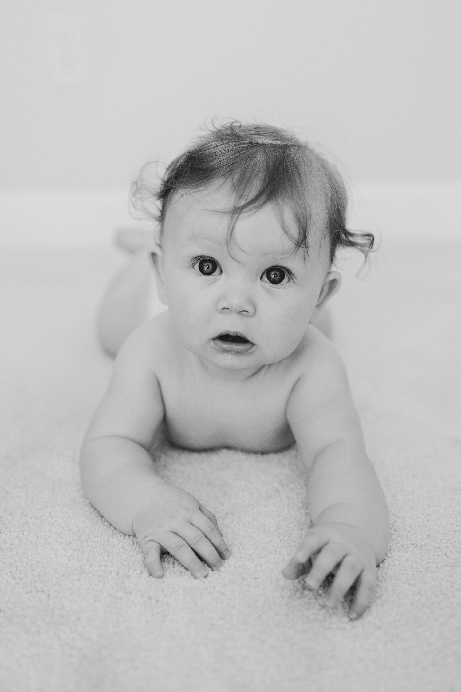 Black and white portrait of baby crawling on textured carpet.