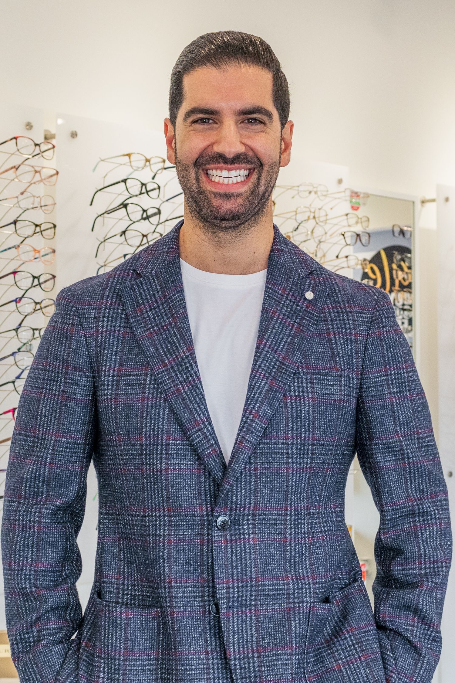 Professional portrait in plaid blazer at optical store with eyewear display.