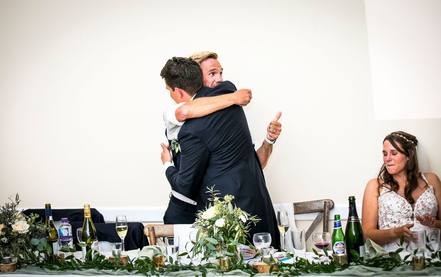 Emotional embrace shared during wedding reception speeches with table decorations in foreground.