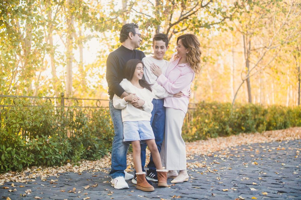 Family portrait captured on a cobblestone path with autumn trees in golden afternoon light.