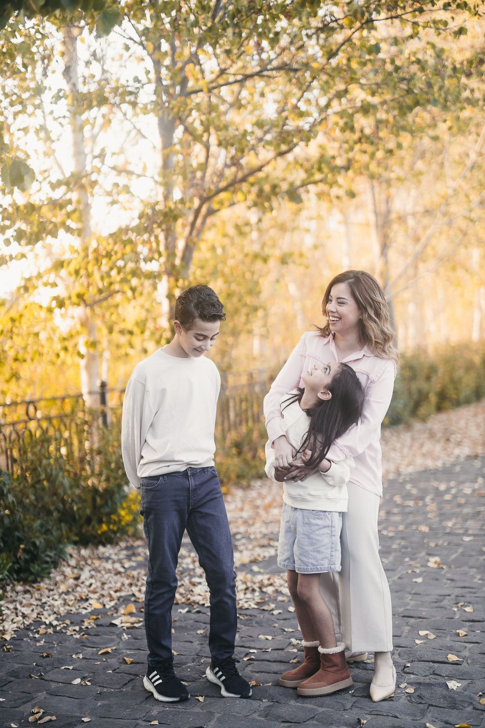 Three people standing on a path surrounded by autumn trees with golden sunlight filtering through.