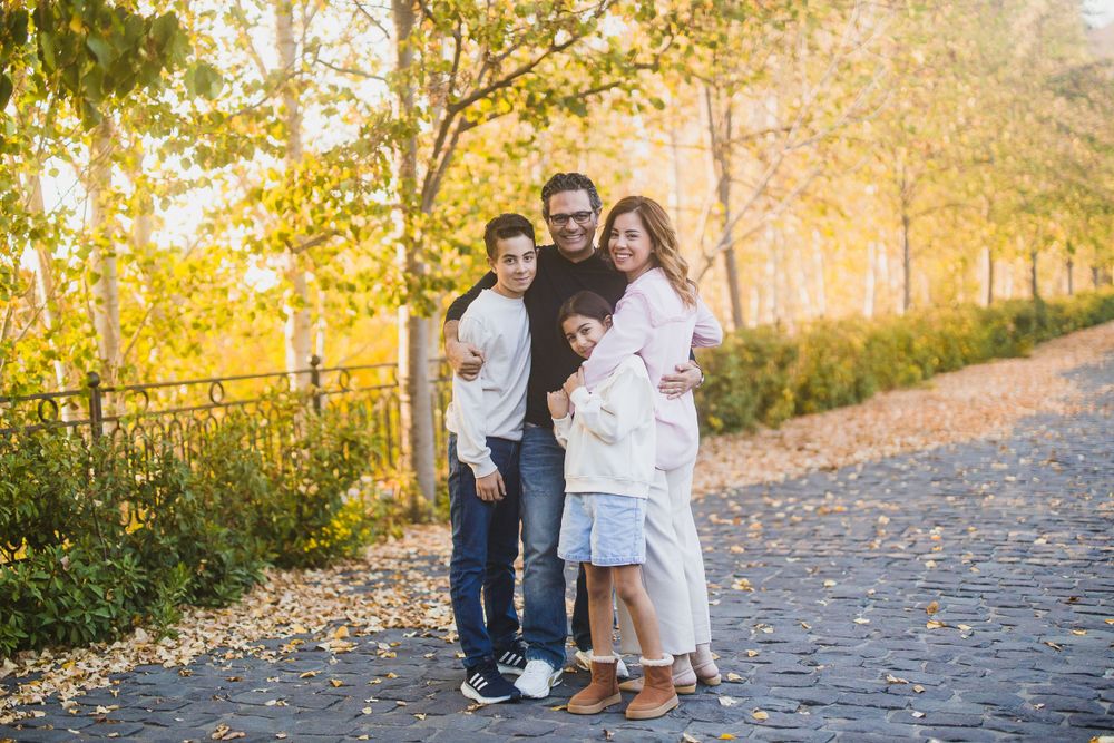 Family standing together on stone pathway with autumn foliage and golden sunset light.