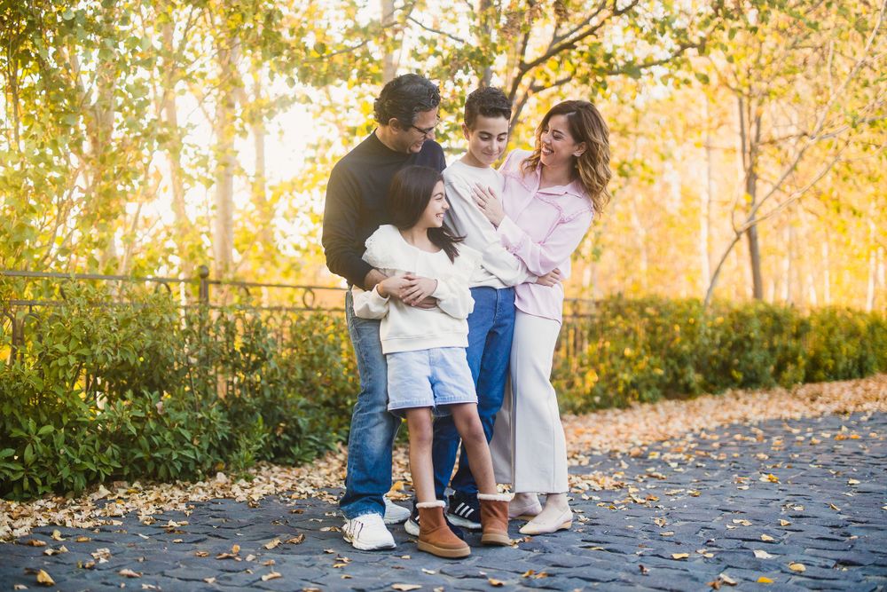 A family embraces while standing on a leaf-covered walkway during fall season.