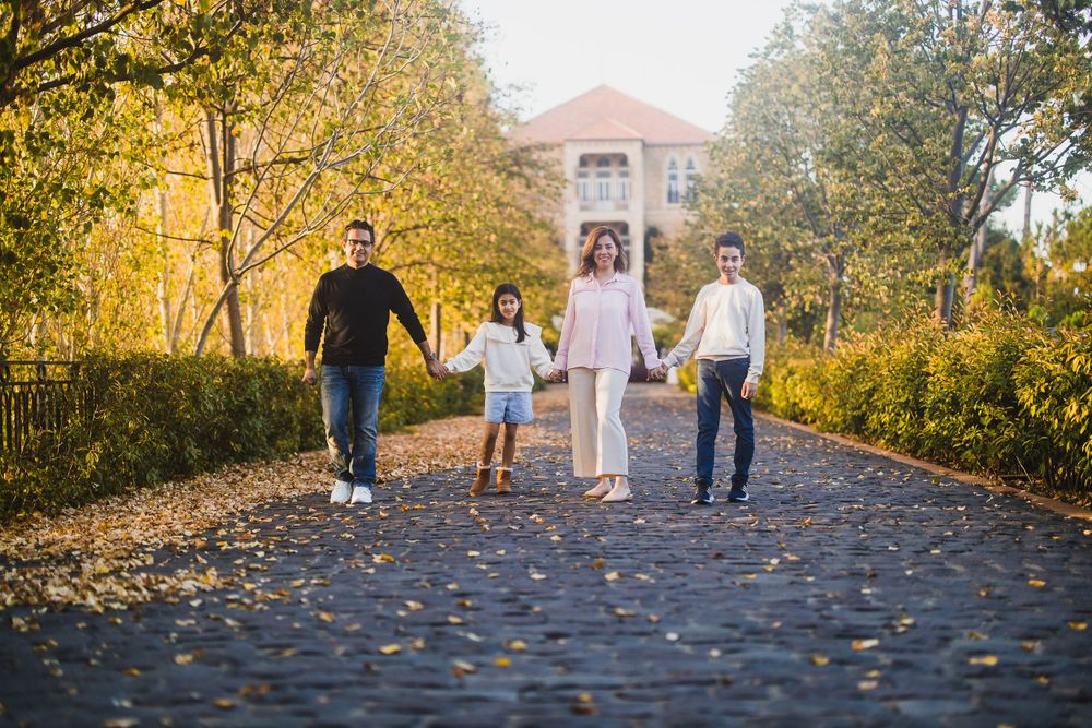 A family strolls together on an autumn path with fallen leaves and golden trees.