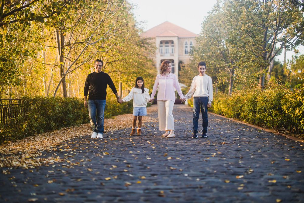 A family of four walks together on a tree-lined path with a pink building in the background.