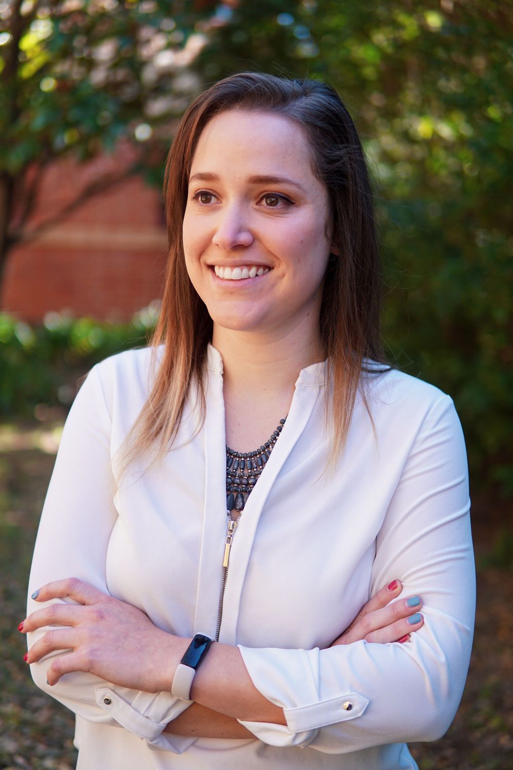 Professional in white blazer with crossed arms standing outdoors near brick building.