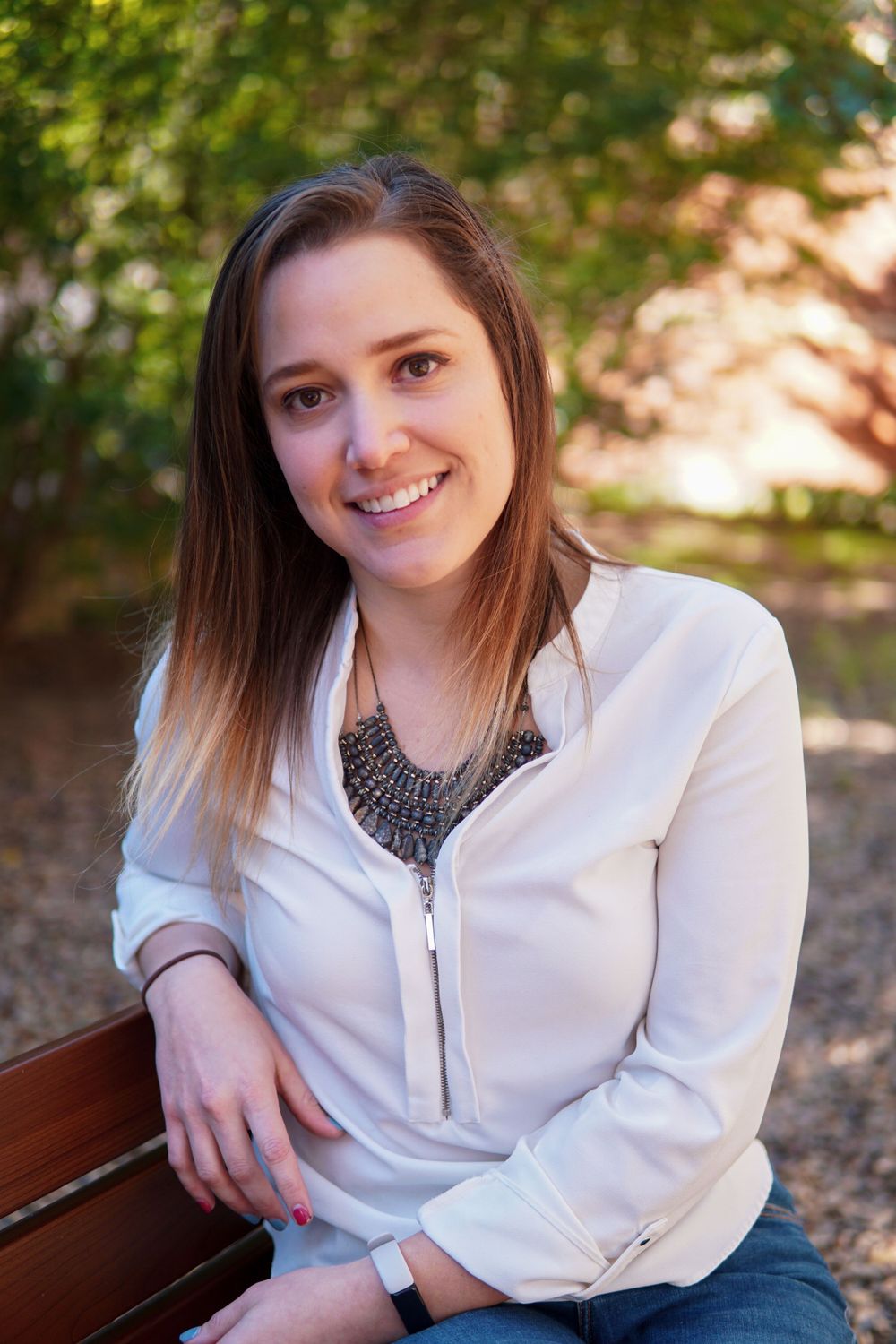 Professional wearing a white blouse with statement necklace sitting on bench in outdoor setting.