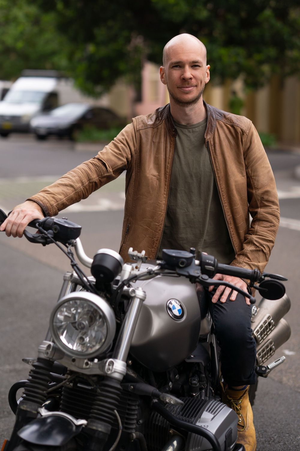 Person in brown jacket posing with BMW motorcycle in parking lot.