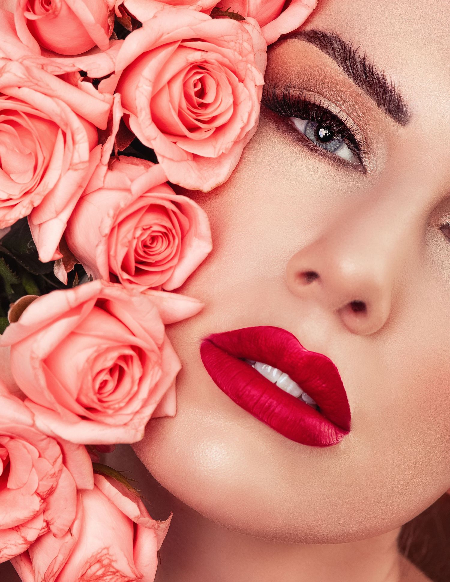 Beauty portrait with coral pink roses and vibrant red lipstick against pink background.